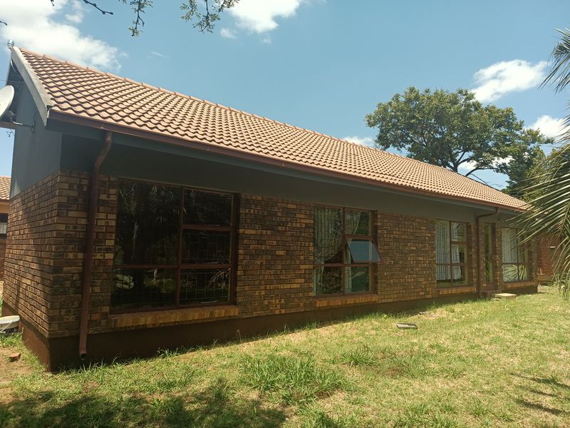 A rear view of a face brick house featuring a tiled roof, aluminium window frames, and established garden surroundings.