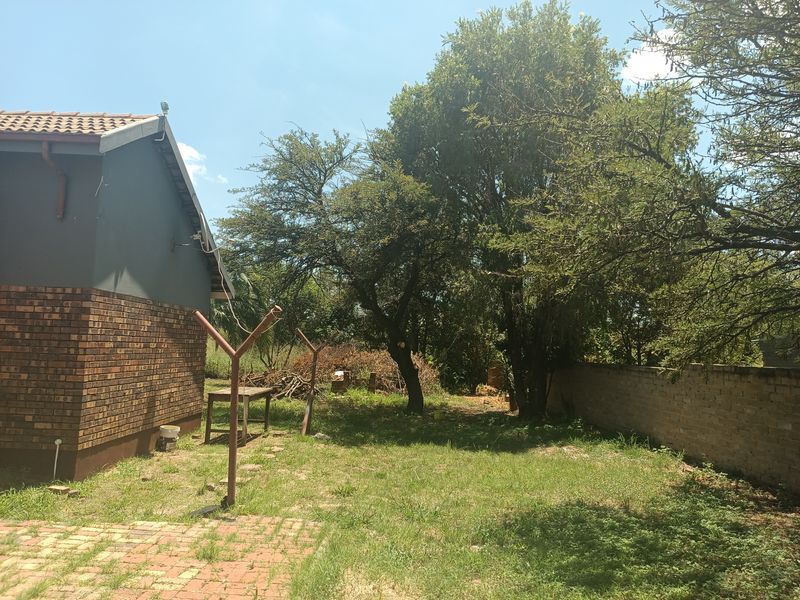 Rear garden area featuring a brick exterior wall, paved patio section, and perimeter walling with mature trees and lawn.