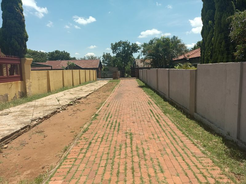 A long brick-paved driveway leading to a gated entrance, flanked by perimeter walls showing signs of wear and weathering.