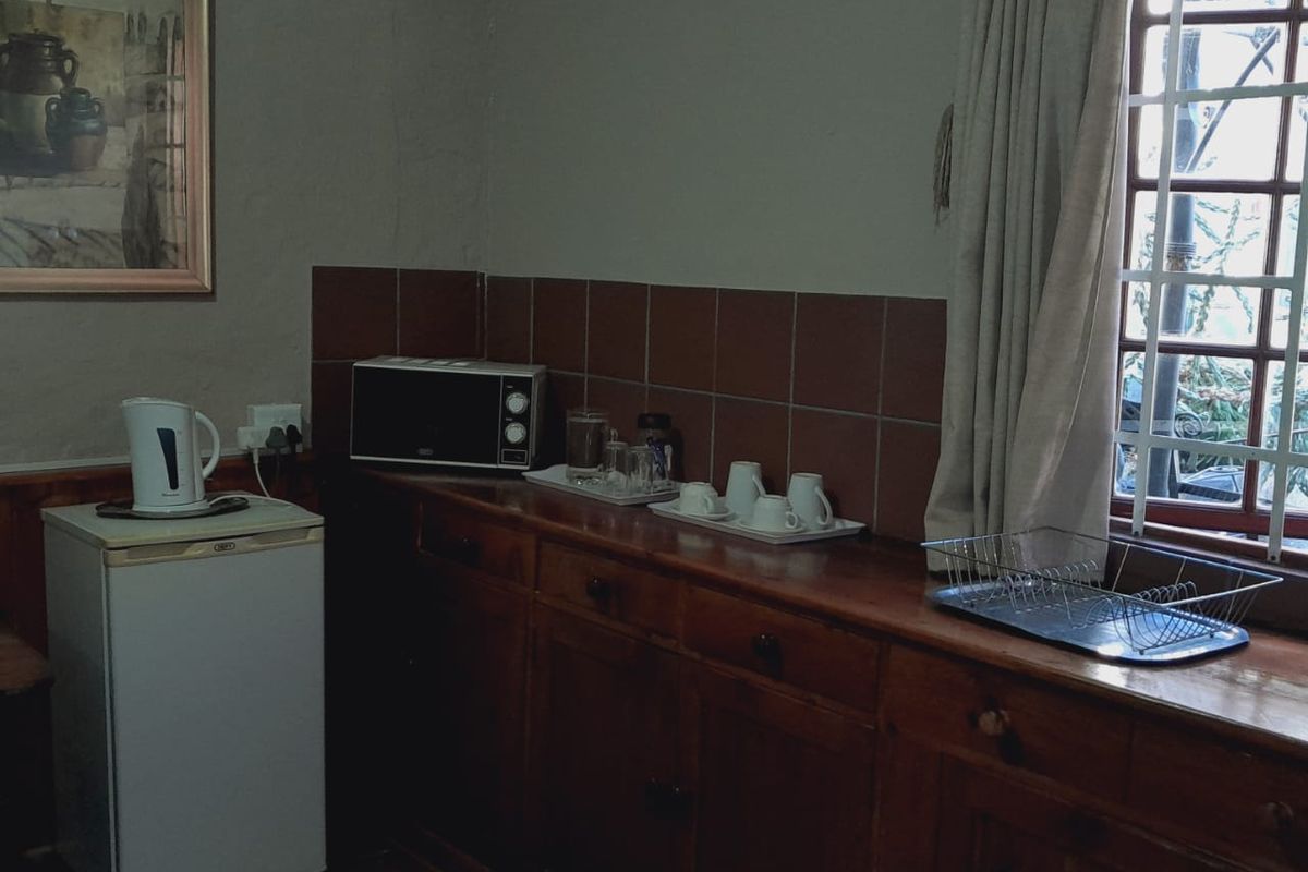 A compact kitchen area featuring wooden cabinetry, tiled backsplash, and tiled flooring, with a window fitted with security bars.