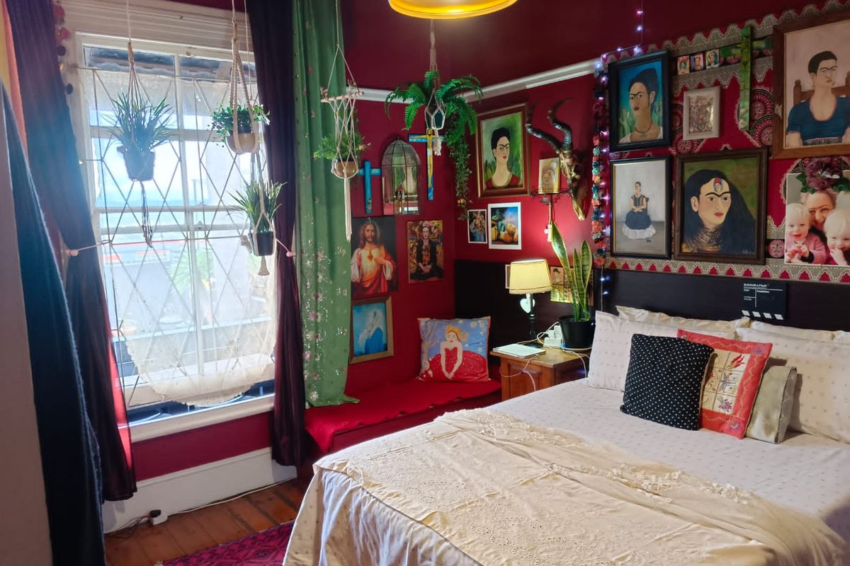 A bedroom featuring timber flooring, a sash window, and a built-in window seat, currently styled with a vibrant, eclectic aesthetic.