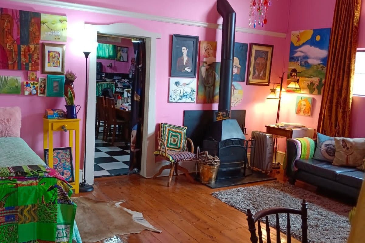 A living room featuring polished hardwood floors, a freestanding wood-burning fireplace, and a decorative chandelier, finished with vibrant pink wall paint.