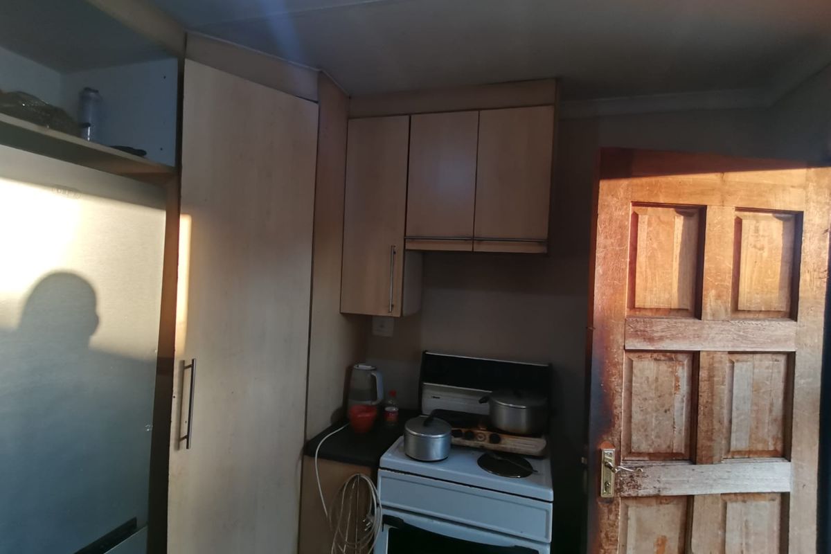 A compact kitchen area featuring built-in cabinetry, a freestanding stove, and a traditional timber door, requiring cosmetic updates to modernize the space.
