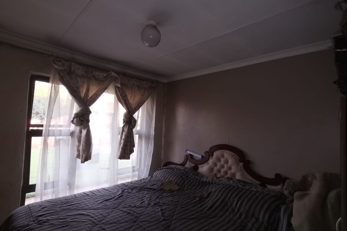 A bedroom featuring a large window with curtains and a simple ceiling light fixture.