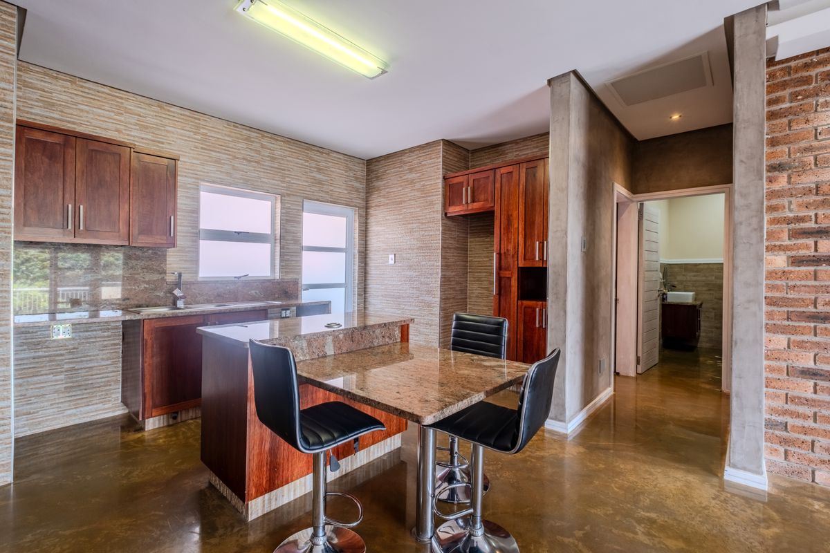 A well-maintained kitchen featuring granite countertops, rich wooden cabinetry, a breakfast bar, and polished concrete floors with an exposed brick accent wall.