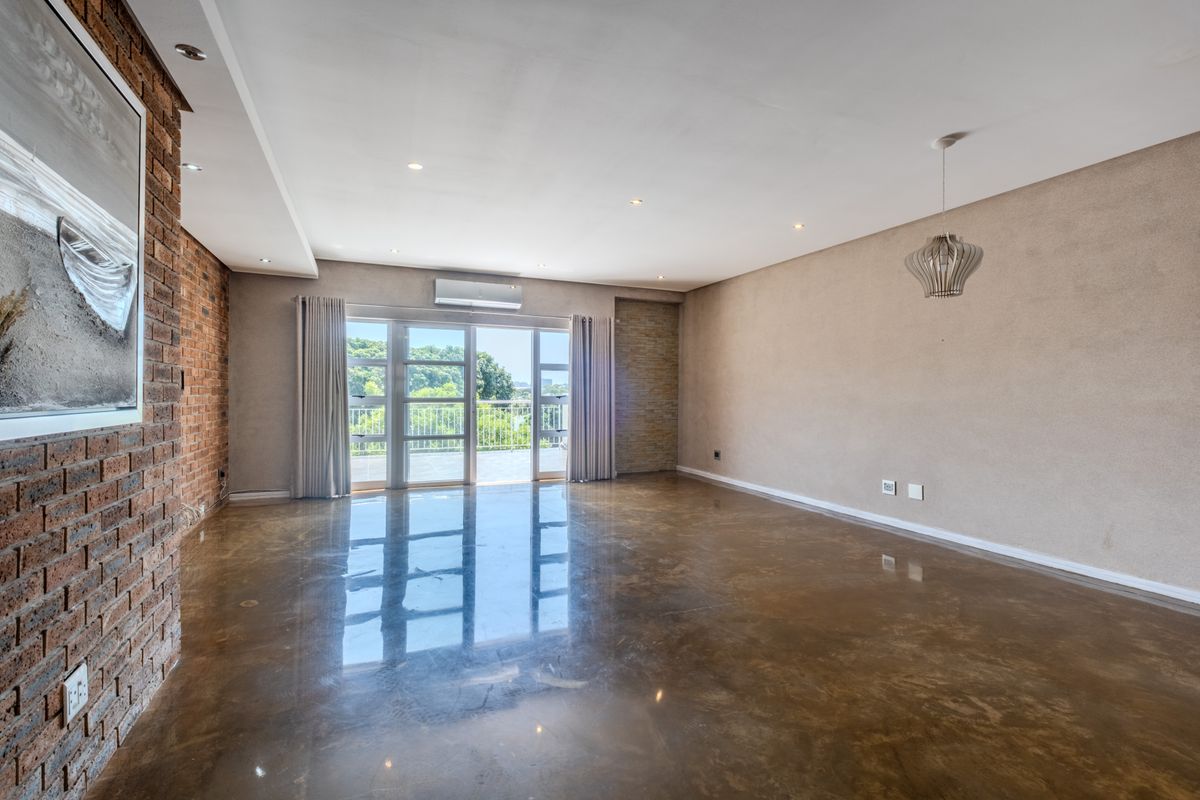 Spacious living area featuring polished concrete floors, an exposed brick feature wall, and large sliding doors leading to a balcony with natural light.