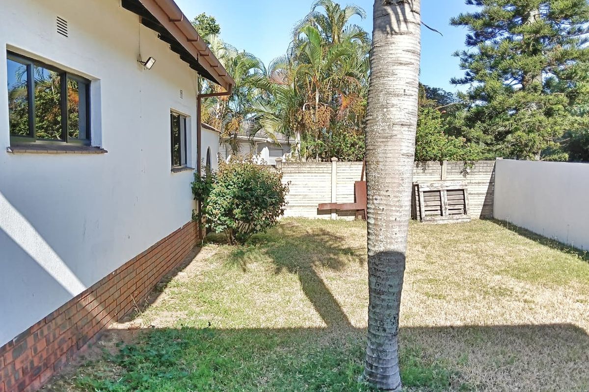 A rear garden area featuring a brick boundary wall, lawn space, and exterior wall access to the main dwelling.