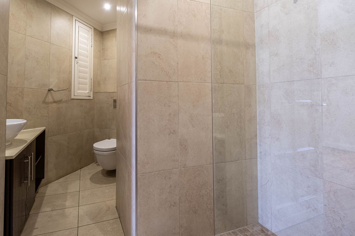 Modern bathroom featuring a wall-mounted toilet, vessel sink vanity, and a spacious walk-in shower with glass screen and neutral floor-to-ceiling tiling.