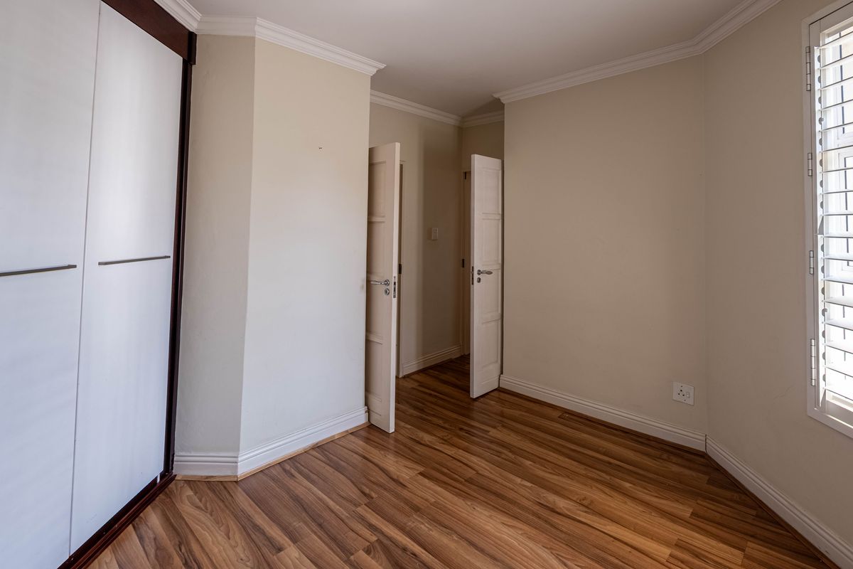 A bright, empty bedroom featuring laminate flooring, built-in wardrobes, and window shutters, offering a clean and neutral space ready for personalization.