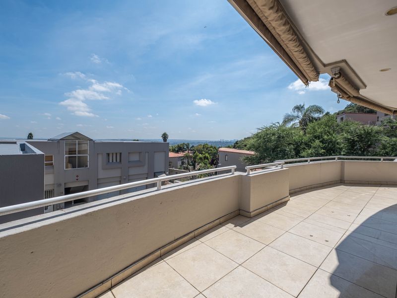 Spacious balcony featuring tiled flooring, a metal balustrade, and a retractable awning, offering elevated views of the surrounding neighborhood.