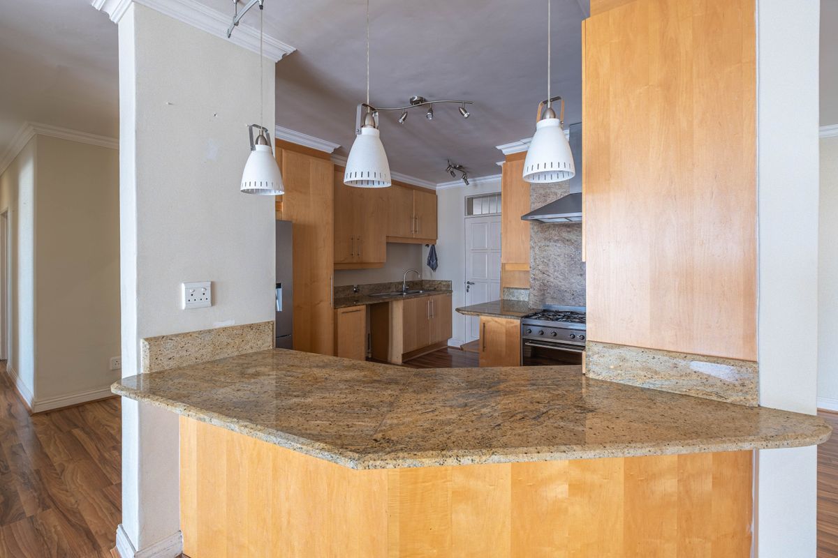 Kitchen featuring granite countertops, wooden cabinetry, gas stove with extractor fan, and laminate flooring, offering a functional layout with breakfast bar.
