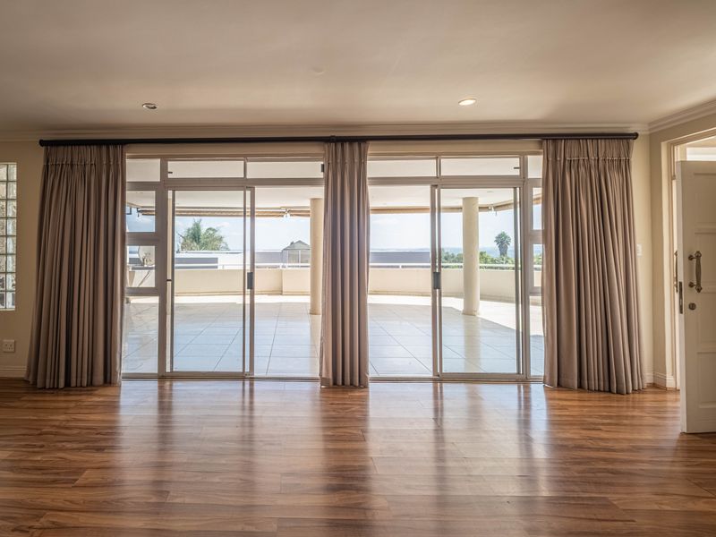Spacious living area featuring laminate flooring, recessed lighting, and large sliding glass doors opening onto a covered balcony with exterior views.