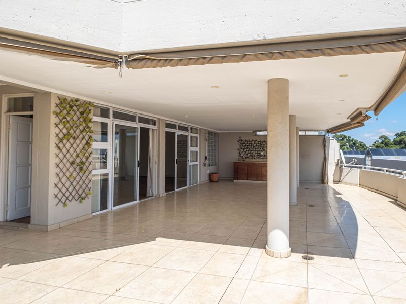 Spacious covered balcony featuring tiled flooring, built-in cabinetry, and retractable awnings, offering a versatile outdoor living area with direct access to the interior.