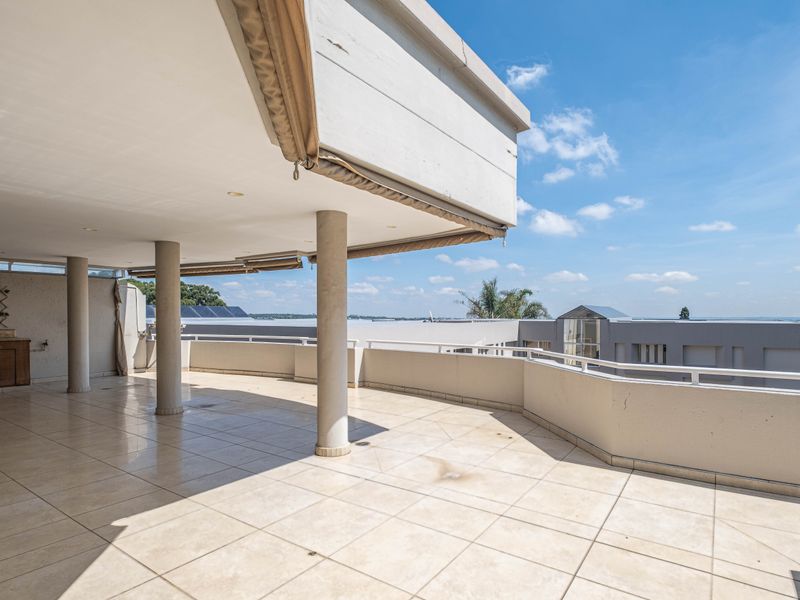 Spacious covered balcony featuring tiled flooring, structural columns, and built-in cabinetry, offering an expansive outdoor area suitable for entertaining.