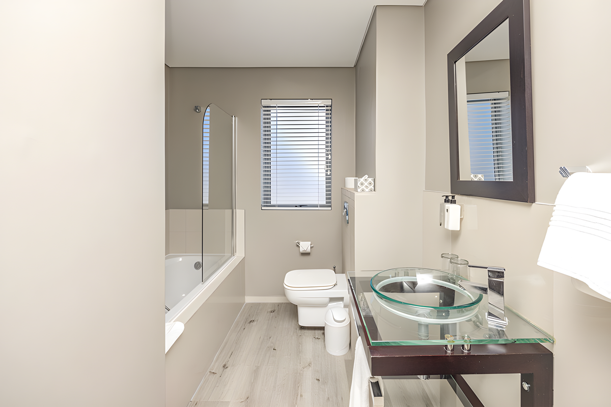 Modern bathroom featuring a glass vessel sink, wall-mounted toilet, and a bathtub with a glass shower screen.