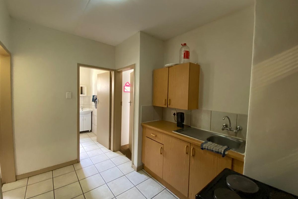 A compact kitchen featuring laminate cabinetry, a stainless steel sink, and tiled flooring, with direct access to adjacent rooms.