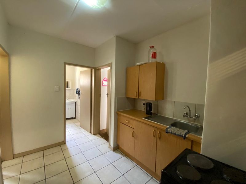 A compact kitchen featuring laminate cabinetry, a stainless steel sink, and tiled flooring, with direct access to adjacent rooms.