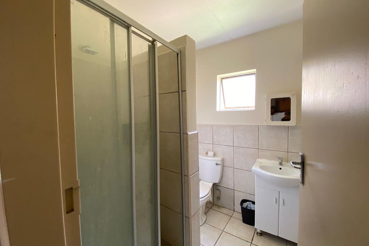 A functional bathroom featuring a shower enclosure, pedestal vanity, and tiled finishes, offering a clean and practical layout.
