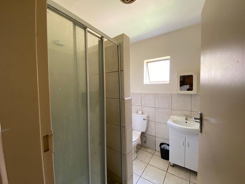 A functional bathroom featuring a shower enclosure, pedestal vanity, and tiled finishes, offering a clean and practical layout.
