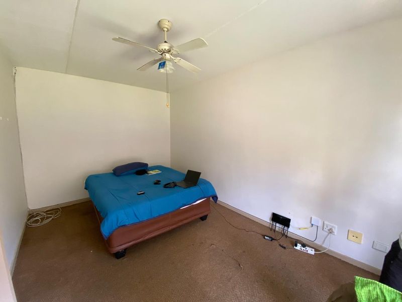 A simple bedroom featuring a ceiling fan and wall-mounted electrical outlets, currently finished with carpet flooring.