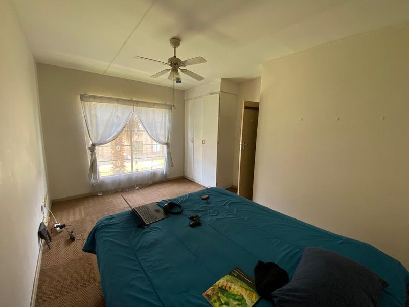 A functional bedroom featuring built-in cupboards, a ceiling fan, and carpeted flooring, offering a neutral canvas for potential updates.
