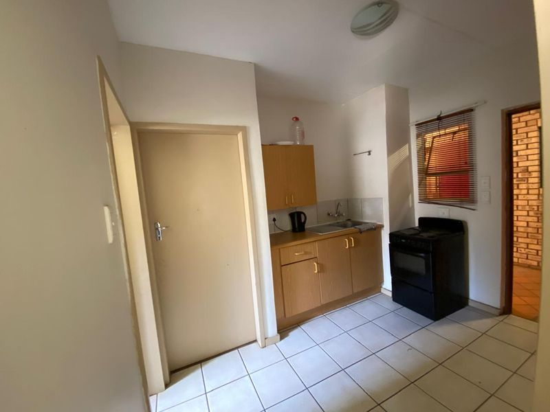 Compact kitchen featuring tiled flooring, built-in wooden cabinetry, a stainless steel sink, and a freestanding stove.