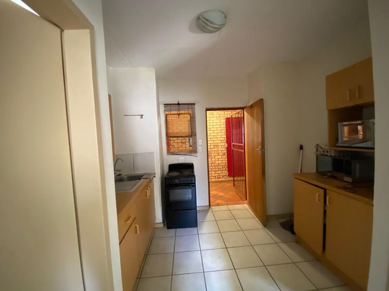 A functional kitchen featuring built-in cabinetry, tiled flooring, and a freestanding stove, with direct access to an exterior area through a security gate.