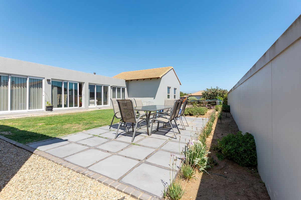 A well-maintained rear exterior featuring a paved patio area, lawn, and boundary wall, providing direct access to the home via sliding glass doors.