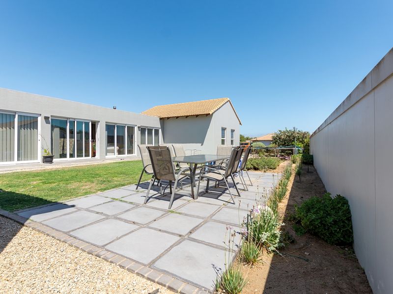 A well-maintained rear exterior featuring a paved patio area, lawn, and boundary wall, providing direct access to the home via sliding glass doors.
