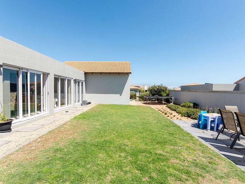 A well-maintained rear garden featuring a paved patio area, a neat lawn, and large sliding glass doors providing seamless indoor-outdoor flow.