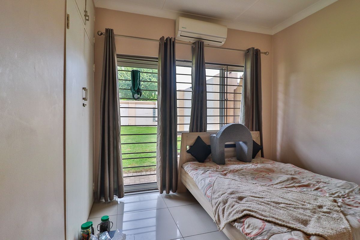 A bedroom featuring tiled flooring, built-in cupboards, a split-system air conditioner, and a sliding glass door with security bars leading to the garden.