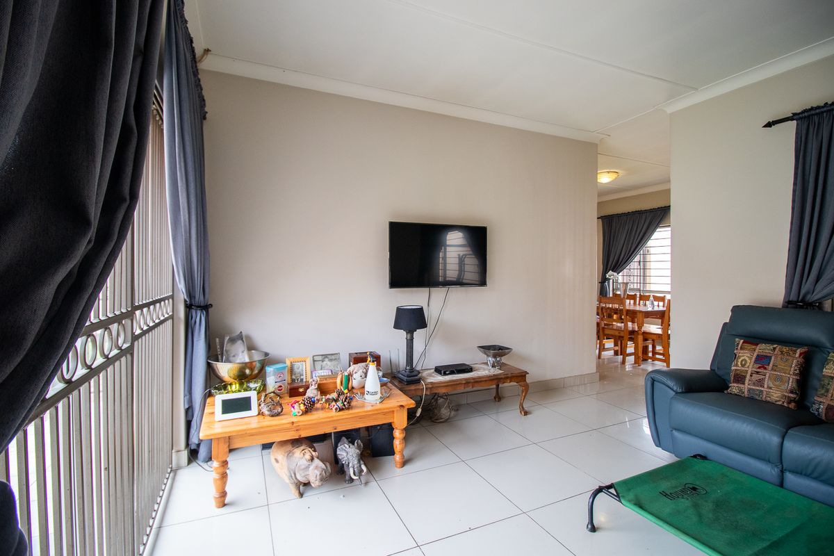 A living room area featuring neutral tiled flooring and coved ceilings, with an open transition to the adjacent dining space.