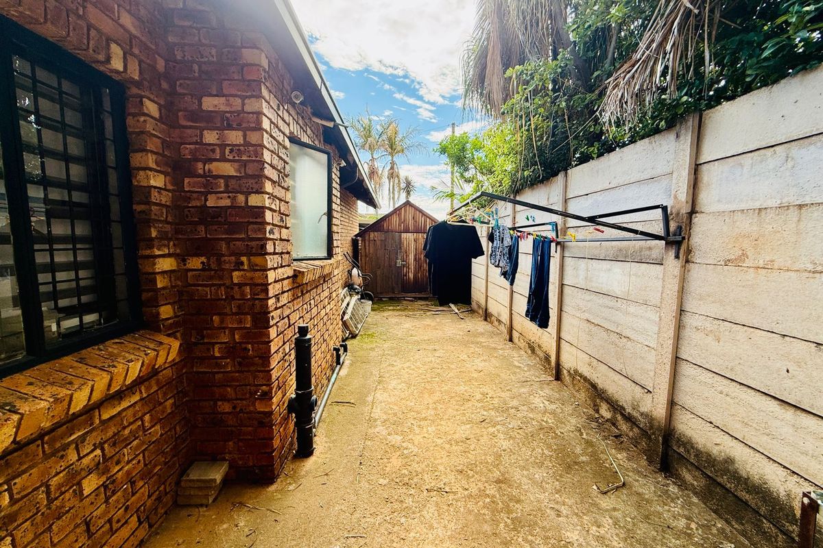 A side exterior area featuring a concrete pathway, brick wall construction, and a precast concrete boundary wall with a small wooden storage shed.
