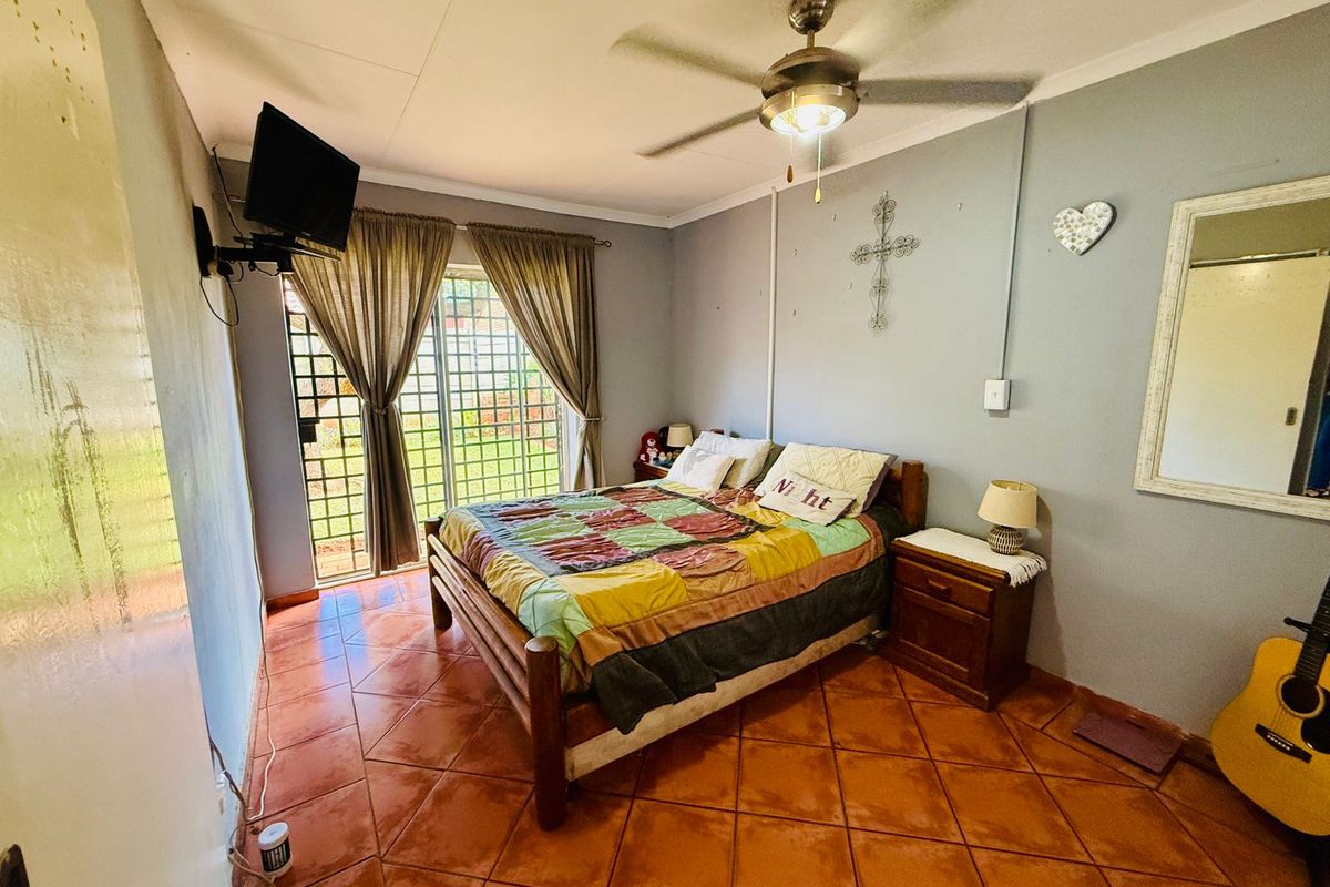 A bedroom featuring terracotta floor tiles, a ceiling fan, and sliding glass doors with security bars providing access to the exterior.