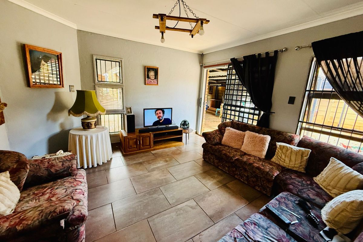 A comfortable living room featuring tiled flooring, a rustic timber chandelier, and large windows with security bars, providing access to an outdoor patio area.