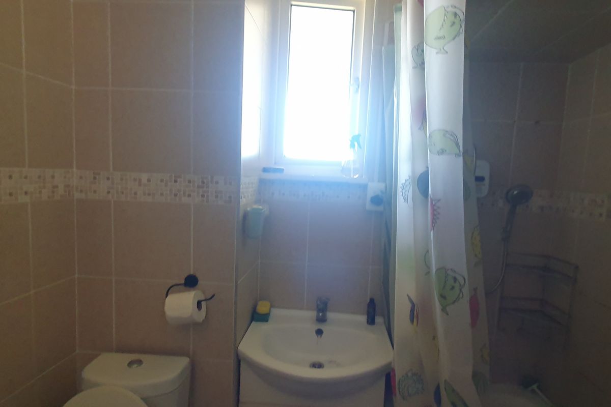 A compact bathroom featuring tiled walls, a pedestal basin, toilet, and a shower area with a window for natural light.