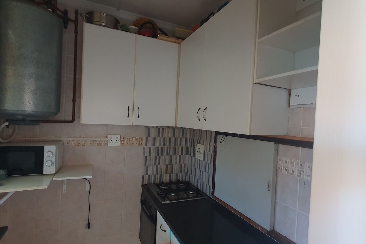 Compact kitchen featuring built-in cabinetry, a gas hob, electric oven, and tiled splashback, with an exposed geyser unit.