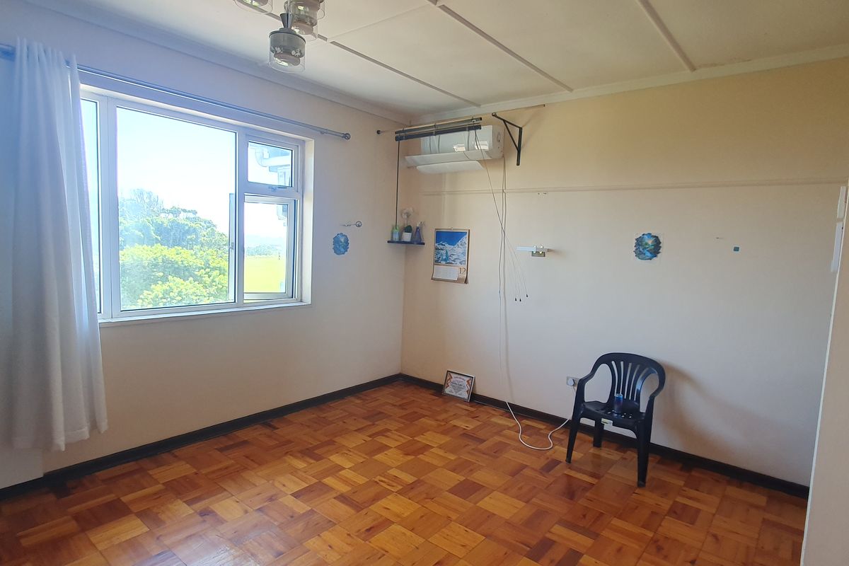 A spacious bedroom featuring parquet flooring, a split-system air conditioner, and large windows providing natural light.