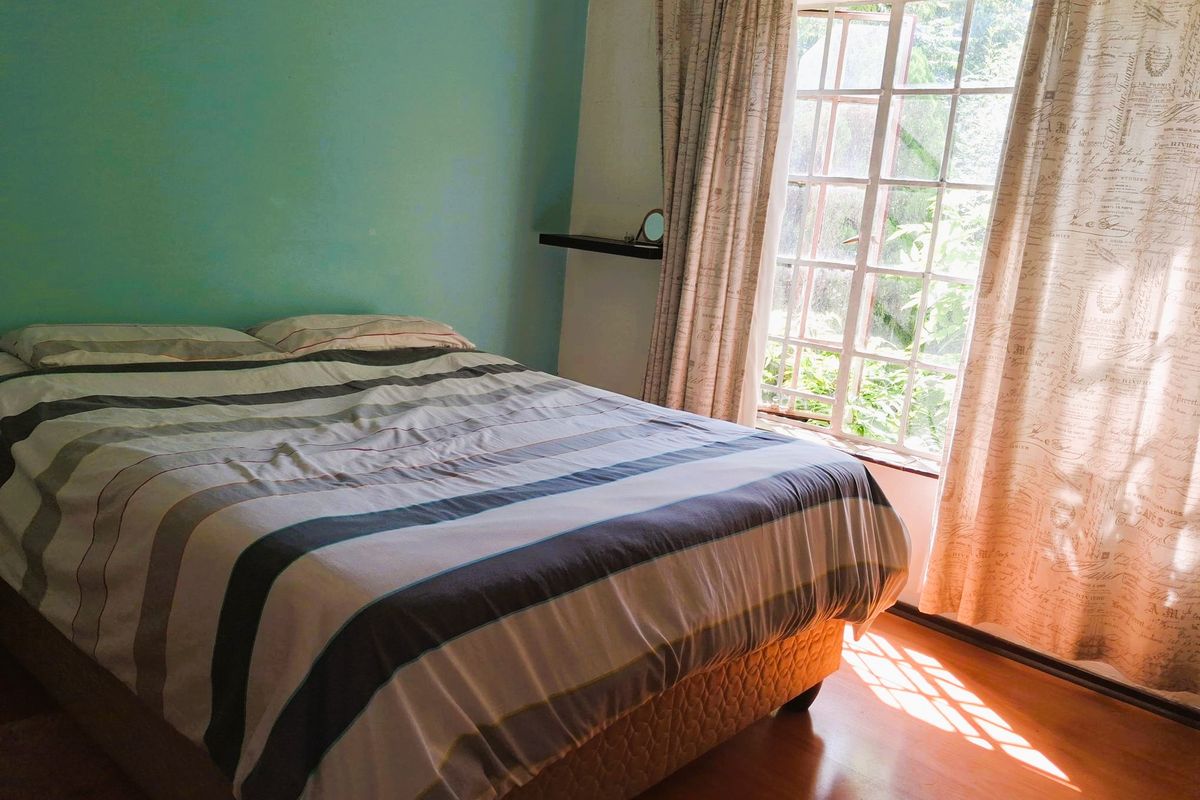 A bedroom featuring laminate flooring, a large window with natural light, and a feature wall.