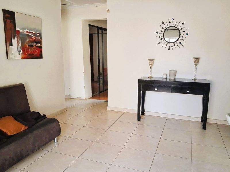 A bright living area featuring neutral ceramic floor tiles and a clear transition into an adjacent room through a doorway.