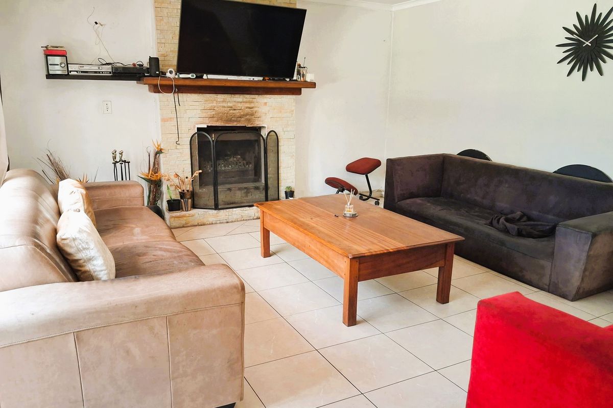 Spacious living room featuring a central stone-clad fireplace with a wooden mantelpiece and neutral floor tiling throughout.