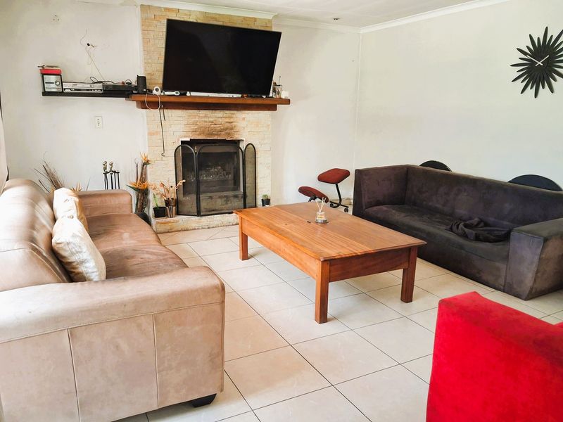Spacious living room featuring a central stone-clad fireplace with a wooden mantelpiece and neutral floor tiling throughout.