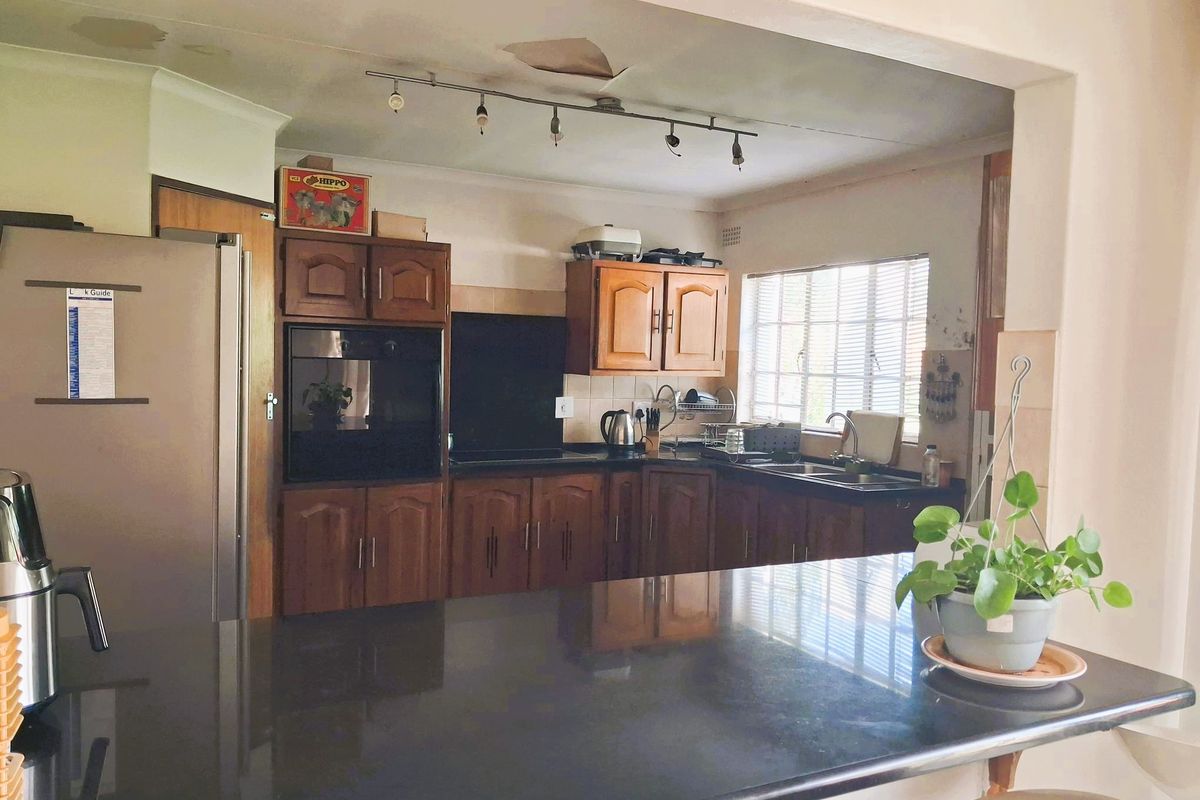 A dated kitchen featuring wooden cabinetry, a dark countertop, and a breakfast bar, with visible ceiling damage requiring repair.