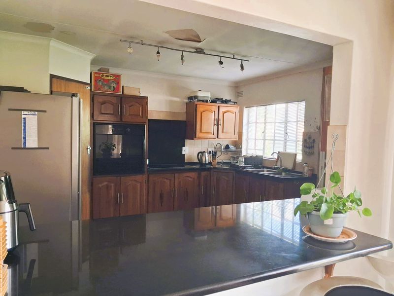 A dated kitchen featuring wooden cabinetry, a dark countertop, and a breakfast bar, with visible ceiling damage requiring repair.