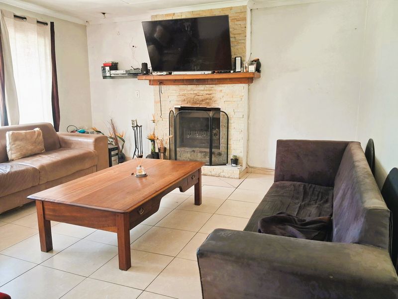 A living room featuring a stone-clad fireplace with a wooden mantel, tiled flooring, and large windows allowing natural light.