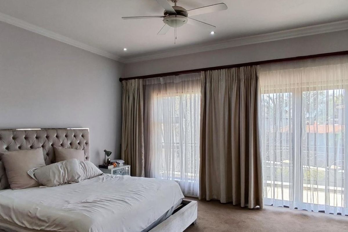 Spacious bedroom featuring neutral wall tones, a ceiling fan, and large glass sliding doors that provide access to an outdoor balcony area.