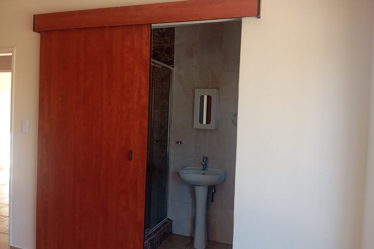 A compact bathroom featuring a pedestal basin, shower enclosure, and tiled finishes, accessed via a wooden sliding door.