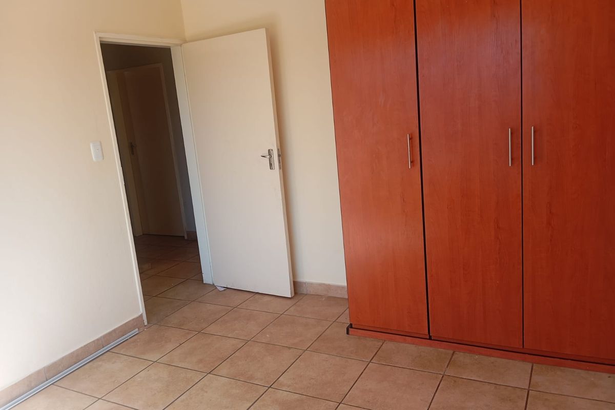 A clean, empty bedroom featuring neutral wall finishes, tiled flooring, and a large built-in wooden wardrobe.