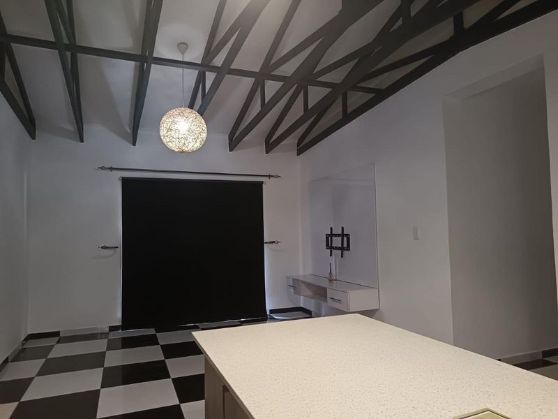 Spacious open-plan living area featuring striking exposed roof trusses, modern checkerboard flooring, and a sleek built-in wall-mounted console unit.