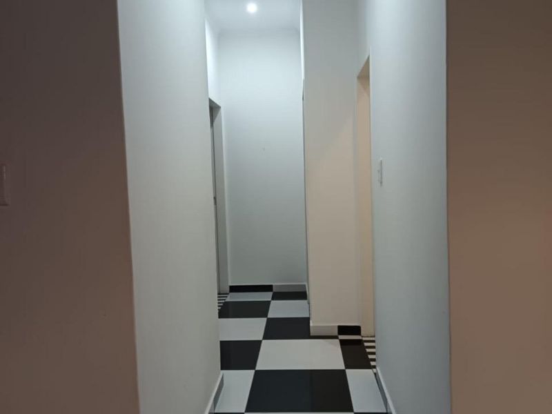 A clean, empty hallway featuring modern recessed downlighting and a distinctive black and white checkered tiled floor.